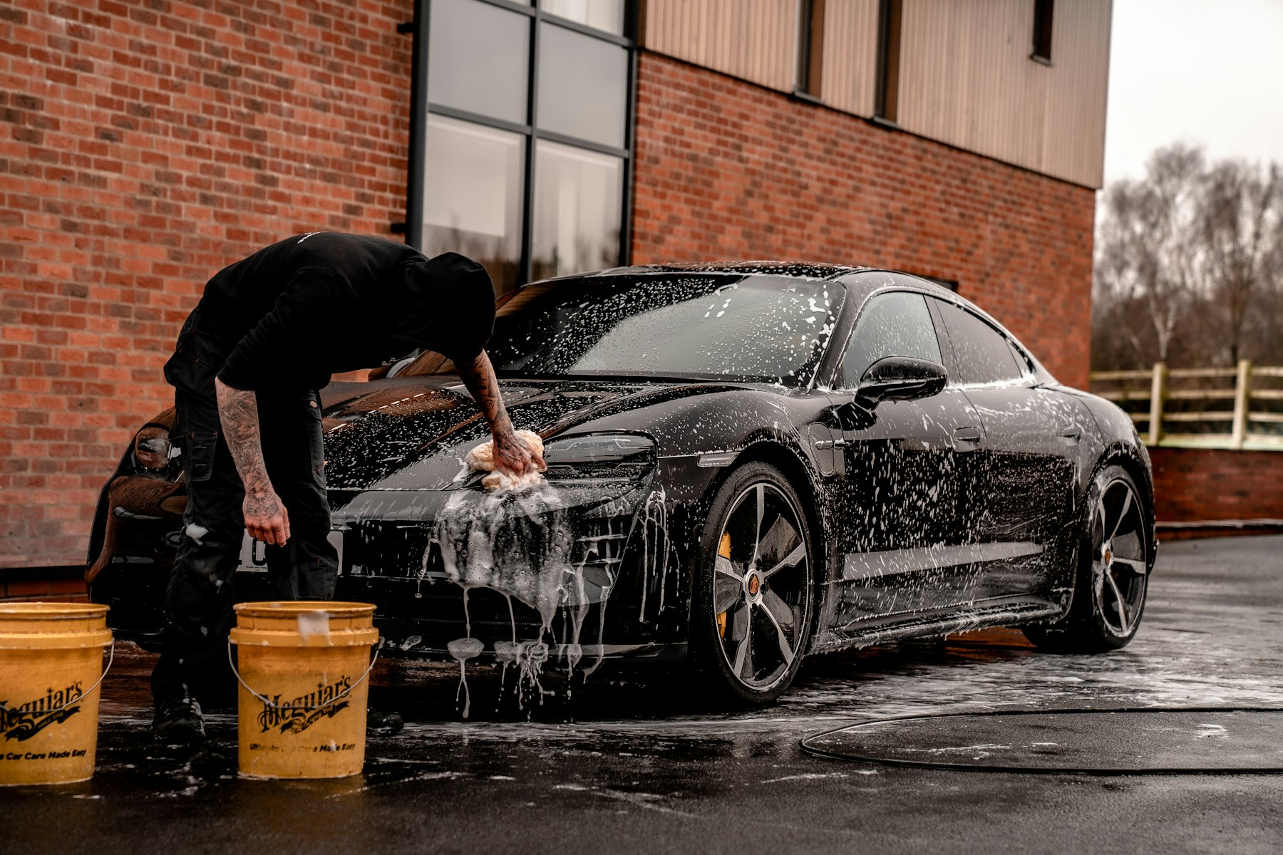 A detailer hand-washing a black car covered in foam