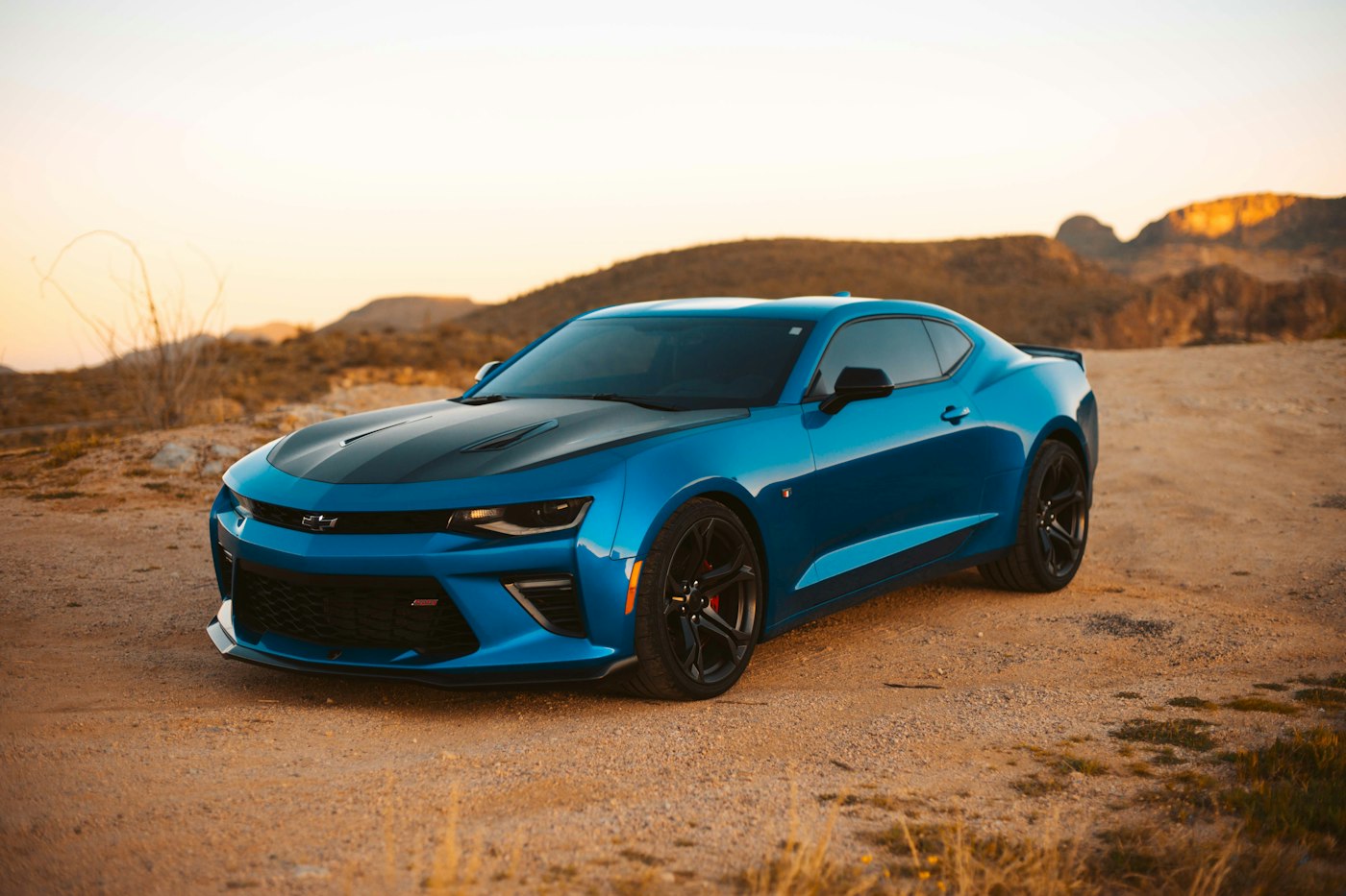 A blue coupe parked in dry, dusty terrain